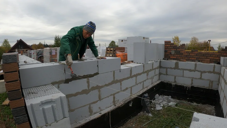 Каменщик выкладывает газобетонную стену внутри контура дома