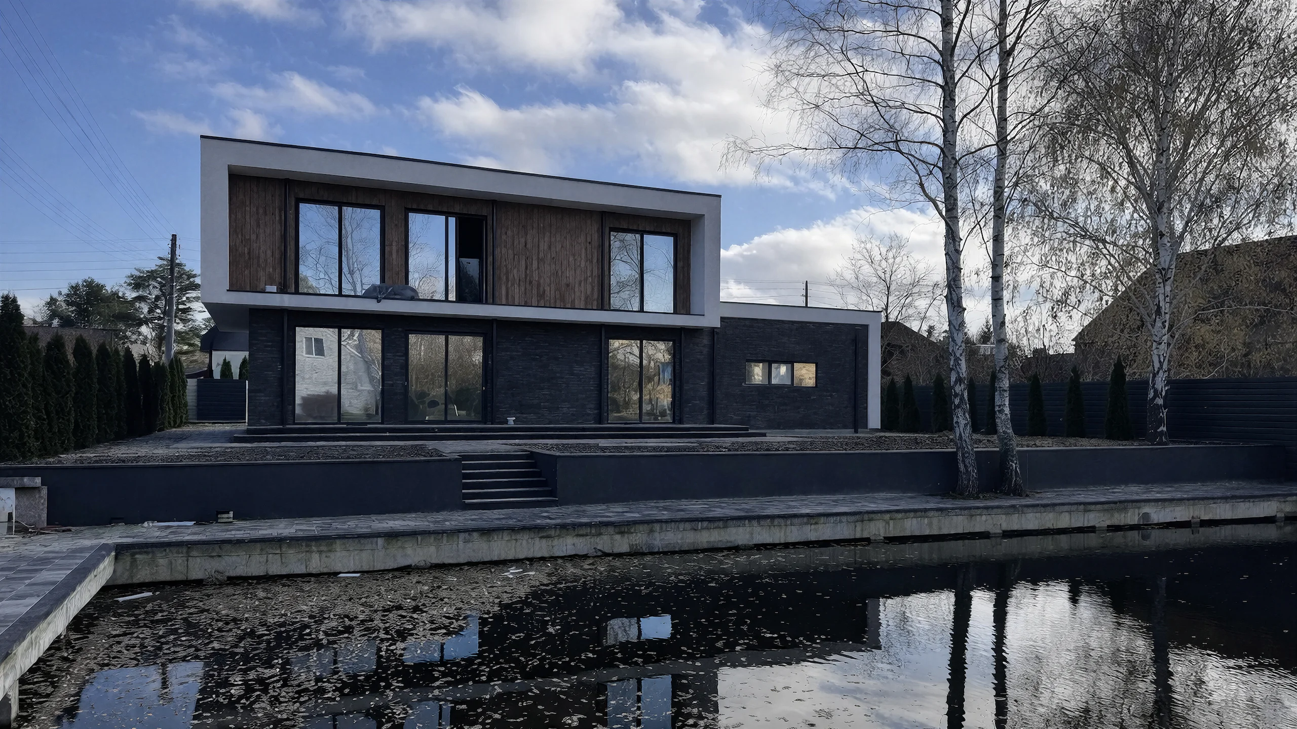 Дворовый фасад двухэтажного дома 429 м² с отражением в воде, панорамными окнами и плоской кровлей