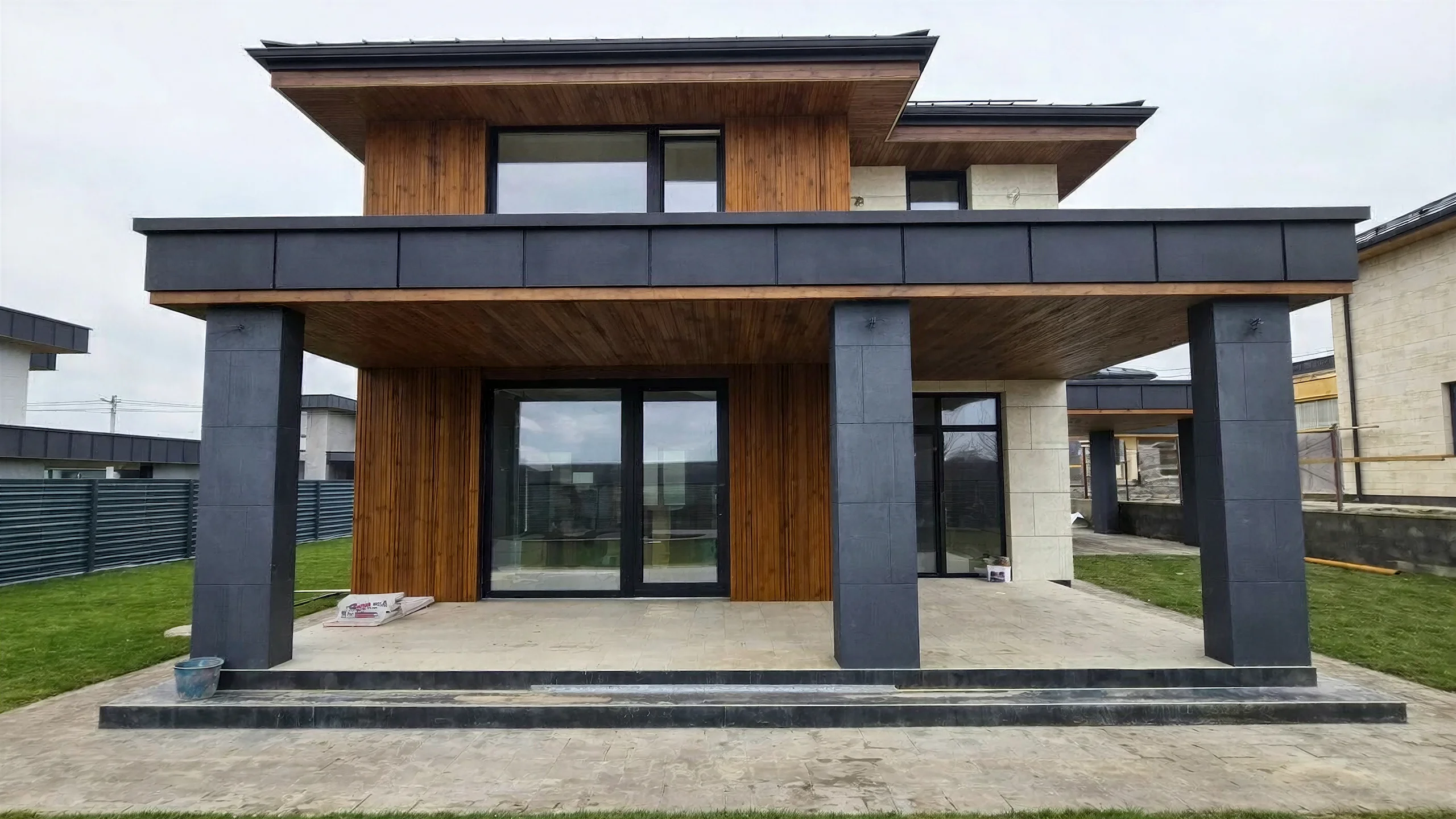 Фасад двухэтажного дома 185 м² с серыми колоннами, деревянными вертикалями и большим остеклением