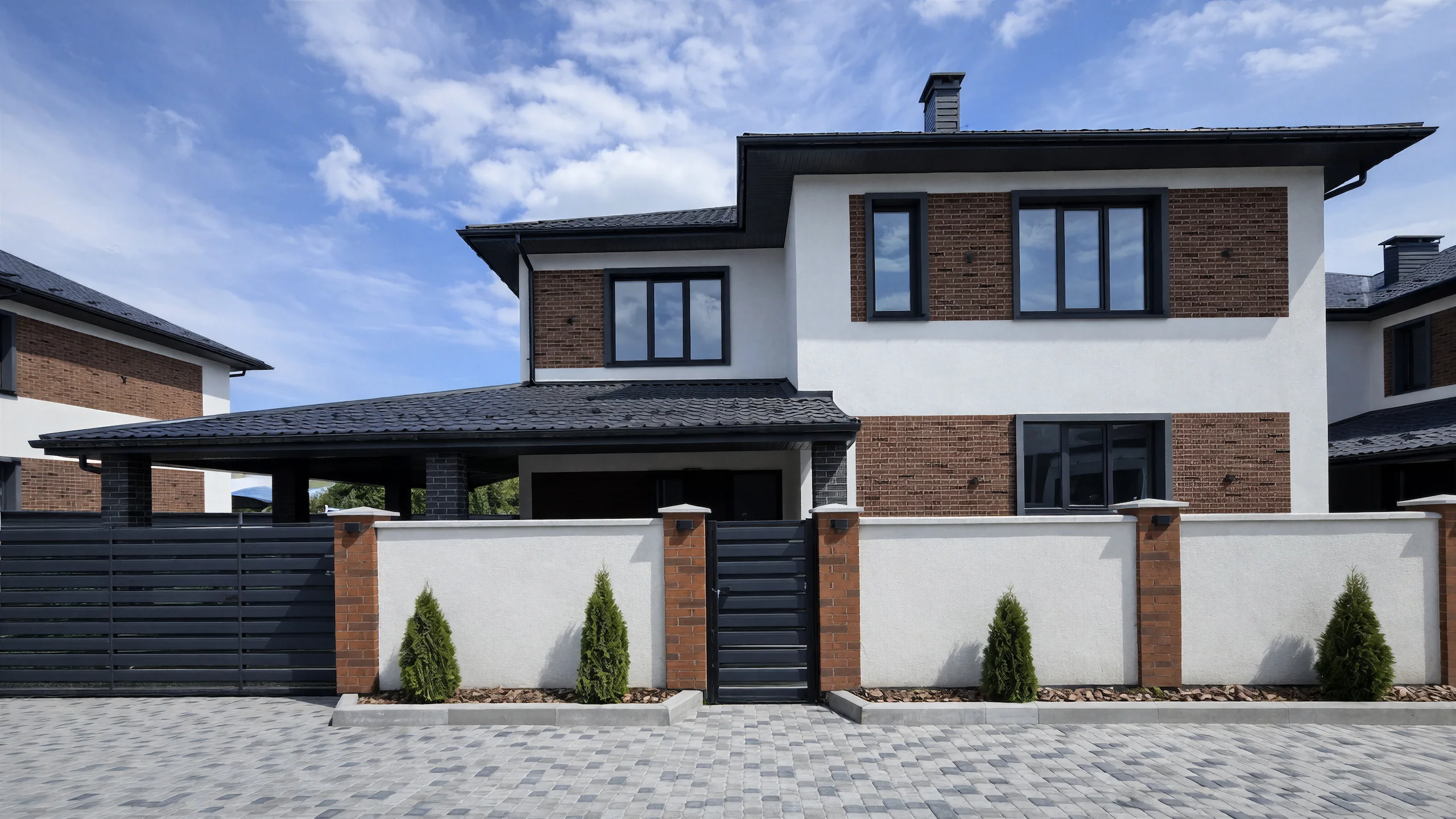 Главный фасад двухэтажного дома 250 м² за каменным забором с белыми стенами и кирпичными акцентами