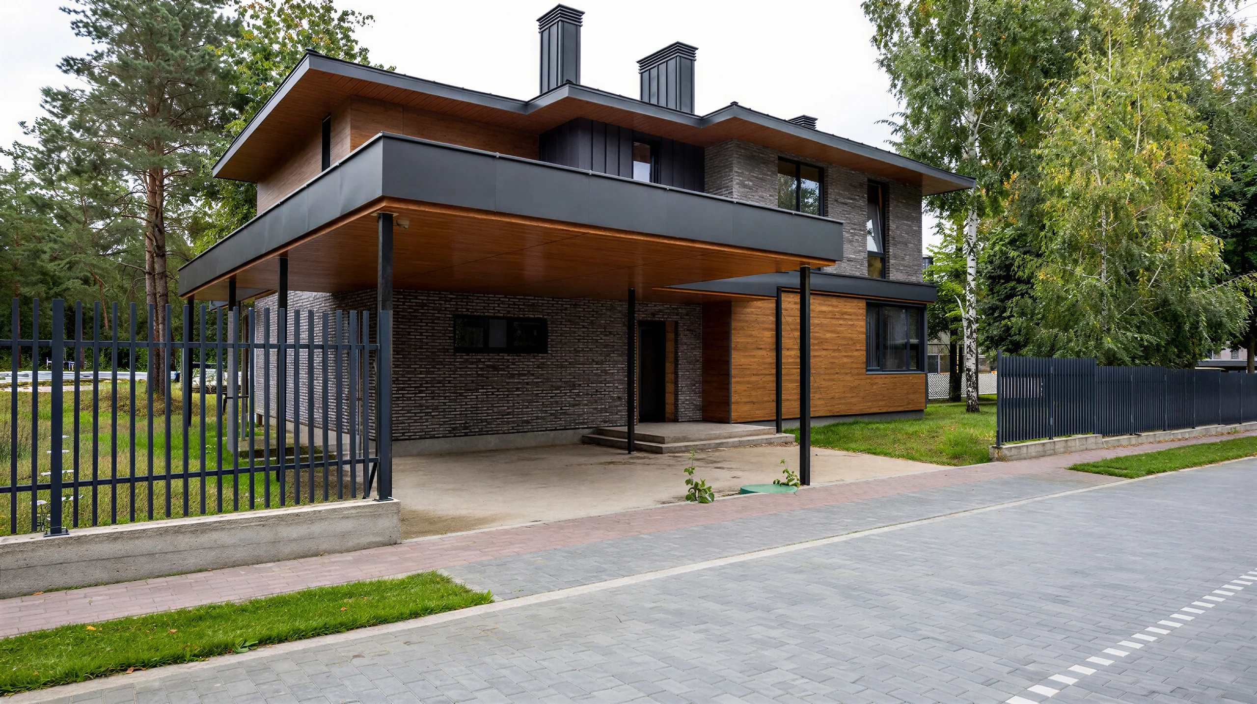 Входная сторона двухэтажного дома 292 м² с широким плоским навесом, серым кирпичом и деревянной отделкой