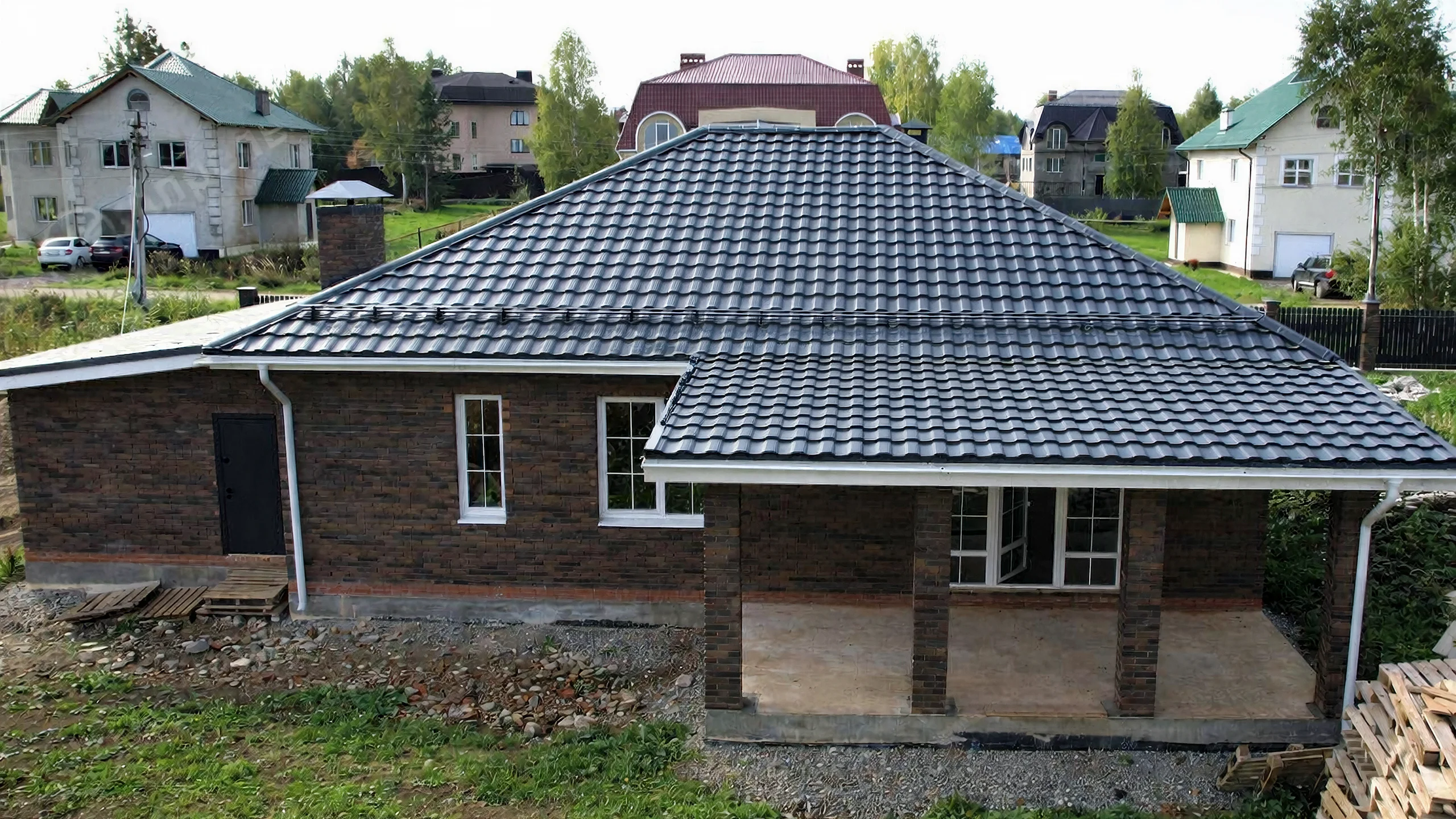 Главный фасад одноэтажного дома 168 м² с белыми наличниками, темной кровлей и кирпичной кладкой