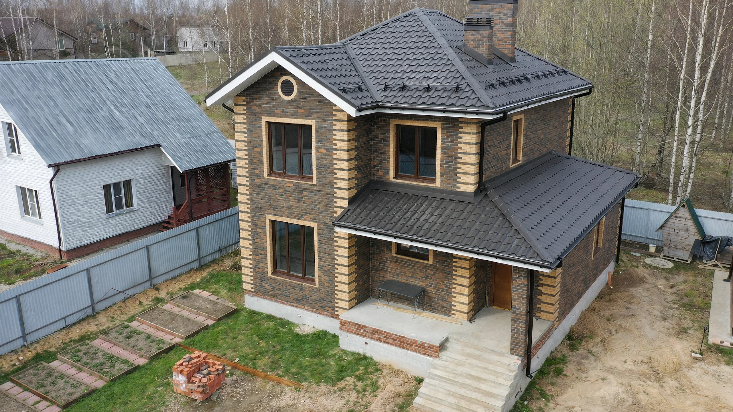 Вид сверху на дом 132 м² с крыльцом, темной кровлей и компактным участком