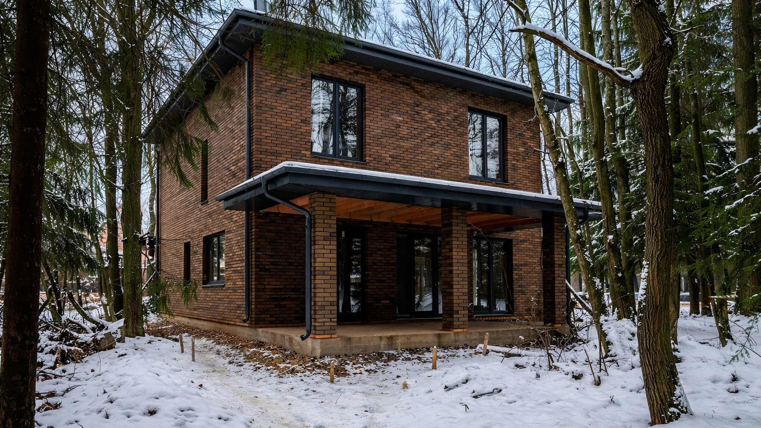 Боковой фасад двухэтажного дома 179 м² с крытым входом, кирпичными стенами и зимним участком