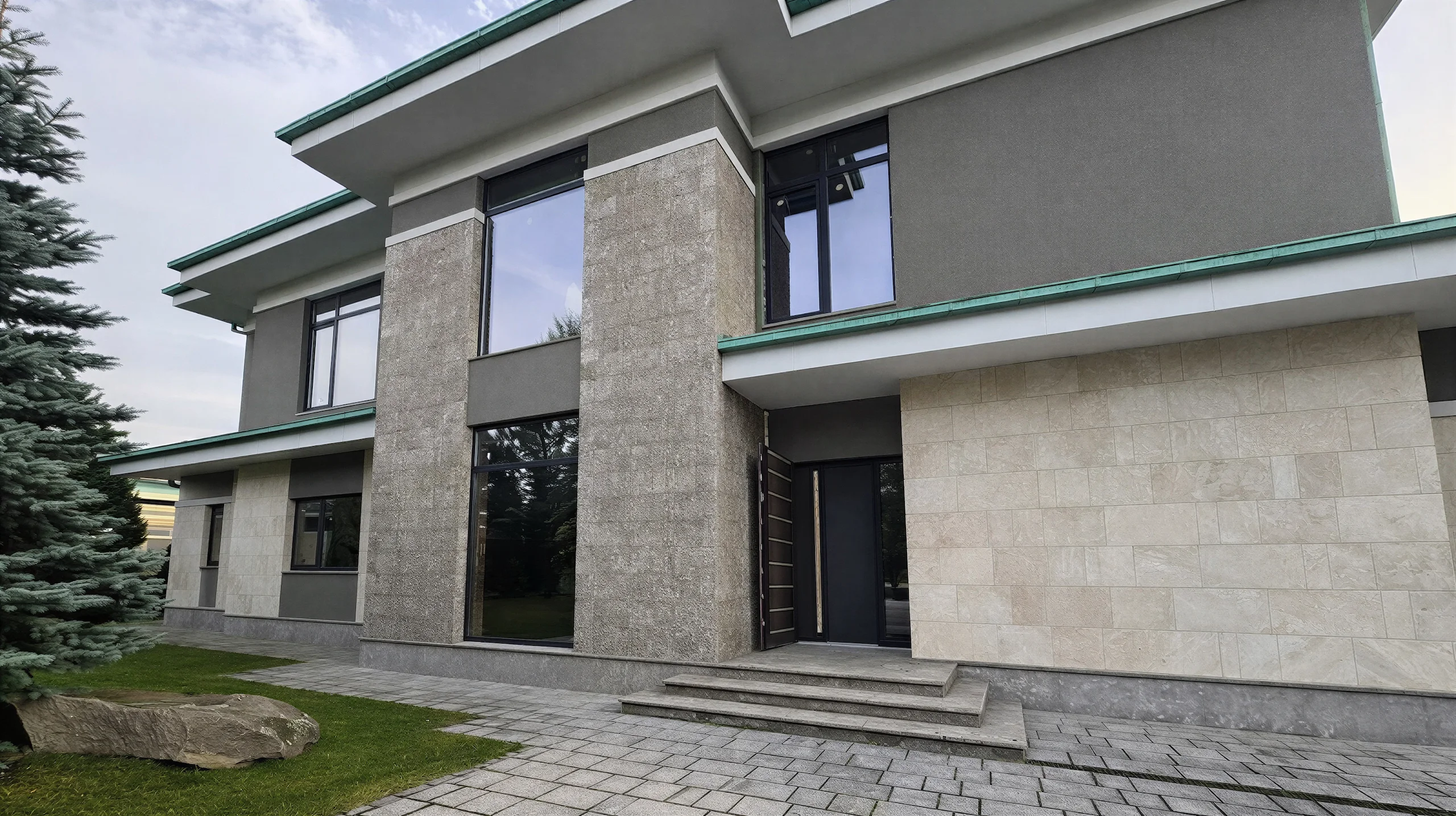 Входная зона двухэтажного дома 478 м² с каменными пилонами, темной дверью и высоким остеклением